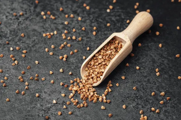 Karabuğday taneleri, ahşap bir kepçeden karanlık bir taşa dökülür..