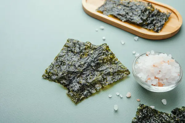 Yeşil arka planda cam kasede tuz bulunan kavrulmuş yosun çerezi.