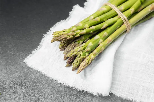Yeşil kuşkonmaz mızrakları toplandı ve bağlandı, dokulu kumaştan bir arkaplanda dinleniyorlar..