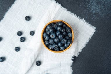 Olgun yaban mersinleri, mutfaktaki beyaz bir bezin üzerinde ahşap bir kasede dizilir..