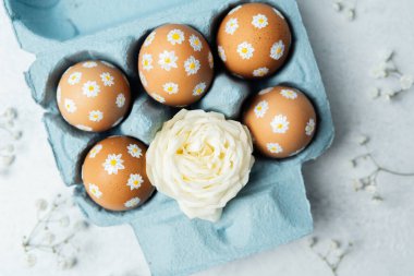 Papatya süslemeli Paskalya yumurtaları ve mavi kartonda beyaz gül. Makro Paskalya detayı arkaplanı.