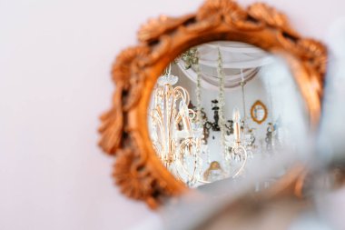 Eski bir ayna şık bir odada süslü bir avizenin parıltısını yakalar..