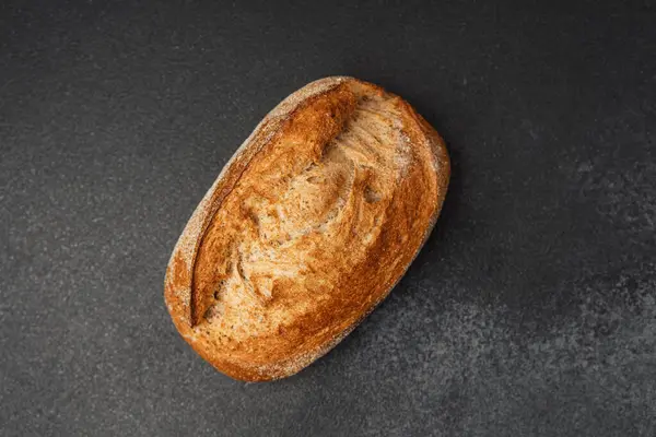 Sıcak, kabuklu bir ekmek somunu koyu bir tezgahın üzerinde duruyor, dokusunu gösteriyor..