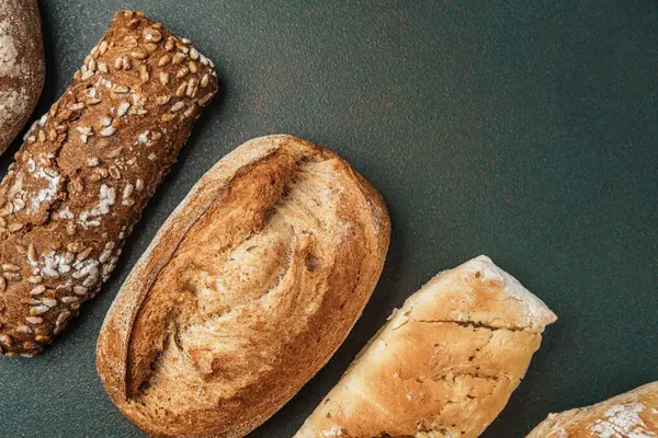 Koyu taş bir yüzeye yerleştirilmiş çeşitli taze ekmek somunları..