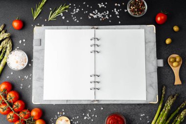 Koyu arkaplanda yemek malzemeleriyle çevrili boş sayfaları olan tarif defteri