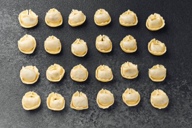 Koyu desenli cerrahi üzerinde ahşap kasede taze çiğ kapel makarna manzarası.