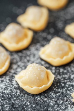 Siyah taş zemin üzerine un serpiştirilmiş taze pişmemiş cappelletti.