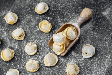 Ahşap kepçeyle un kaplı koyu arkaplanda çiğ kapel makarna.