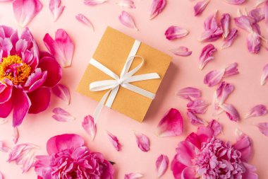 Beyaz kurdeleli hediye kutusu ve pastel arka planda pembe şakayık çiçekleri dağınık taç yapraklarıyla