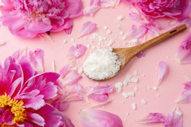 Ahşap kaşık soya yağı tanecikleri ve pembe arka planda pembe şakayık yaprakları.