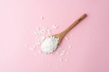 Ahşap kaşık, temiz pembe arka planda soya yağı tanecikleri.