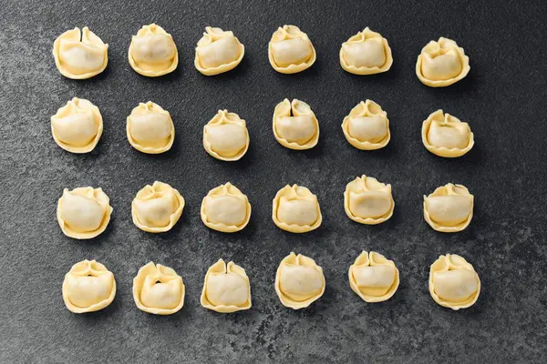 Koyu desenli cerrahi üzerinde ahşap kasede taze çiğ kapel makarna manzarası.