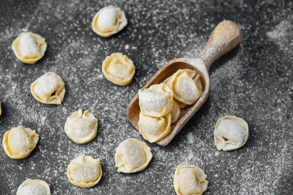 Ahşap kepçeyle un kaplı koyu arkaplanda çiğ kapel makarna.