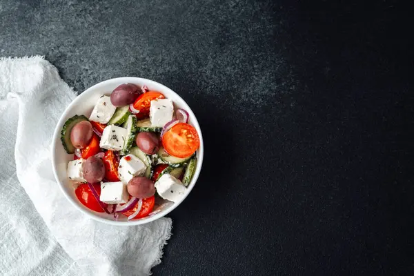 Yunan salatası, peynirli salatalık, salatalık, domates ve soğan, koyu arkaplanda, peçeteli beyaz kasede.