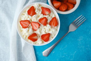 Bir kase süzme peynir, çilekli ve çatallı mavi ördek.