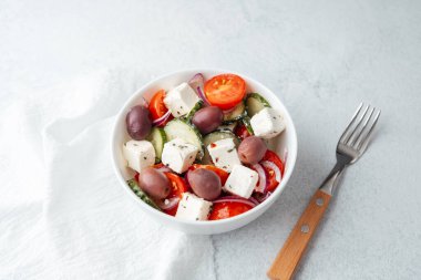 Fettan peynirli Yunan salatası, salatalık ve çatallı beyaz kâse içinde domatesler.
