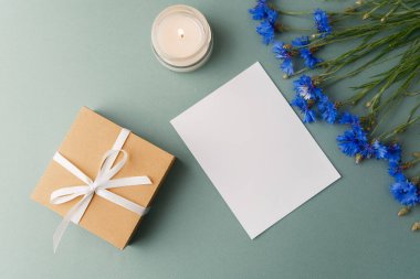Yeşil arka planda çiçek olan hediye kutusu, mum ve kart