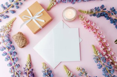 Kurdeleli hediye kutusu, zarf, çiçekler ve pembe arka planda mum.