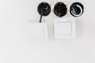 Bitmemiş duvarda açık kablolar olan iki beyaz elektrik düğmesi.