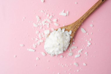 Ahşap kaşık, temiz pembe arka planda soya yağı tanecikleri.