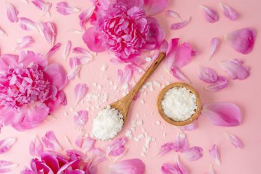 Ahşap kaşık ve kase, pembe yapraklarla çevrili soya mumu taneleri.