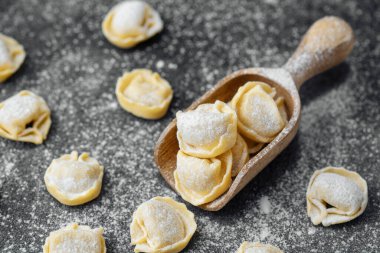 Ahşap kepçeyle un kaplı koyu arkaplanda çiğ kapel makarna.