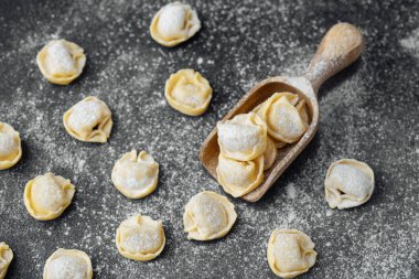 Ahşap kepçeyle un kaplı koyu arkaplanda çiğ kapel makarna.