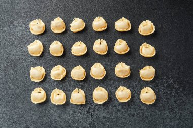 Koyu desenli cerrahi üzerinde ahşap kasede taze çiğ kapel makarna manzarası.