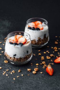 Yoğurtlu granola parfe, koyu arkaplanda çilek ve yabanmersini.
