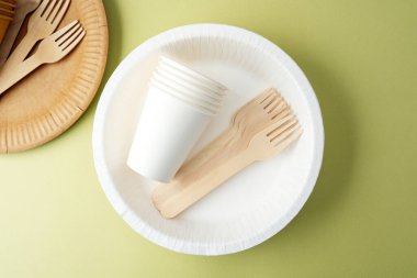 Yeşil zemin üzerine dağılmış çevre dostu kağıt bardaklar ve çatallar