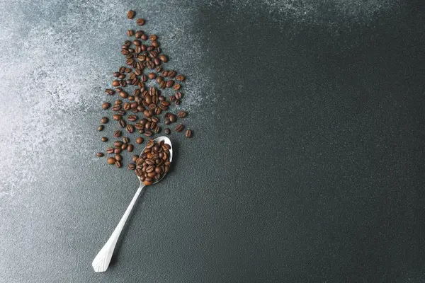 Koyu arkaplanda metal kaşıkta kahve çekirdekleri