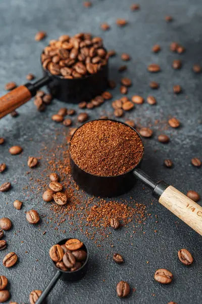 Koyu arka plandaki kepçeleri ölçmek için öğütülmüş kahve ve fasulye.