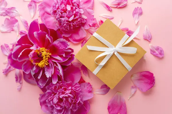 Beyaz kurdeleli hediye kutusu ve pastel arka planda pembe şakayıklar.