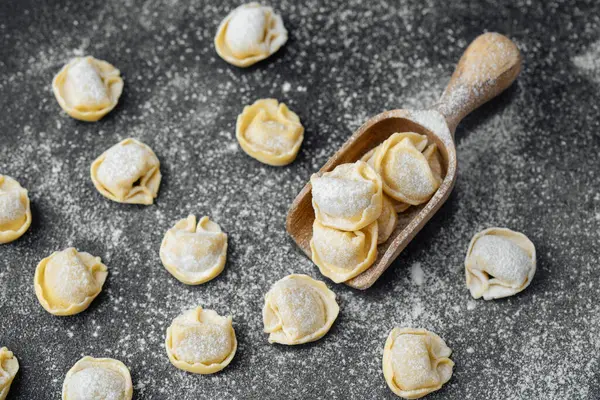 Ahşap kepçeyle un kaplı koyu arkaplanda çiğ kapel makarna.