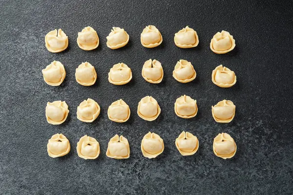 Koyu desenli cerrahi üzerinde ahşap kasede taze çiğ kapel makarna manzarası.