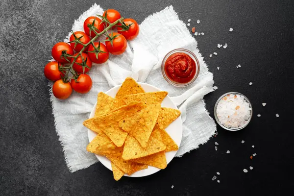 Taze domatesli nacho, beyaz örtülü salsa ve tuz koyu arkaplanda.