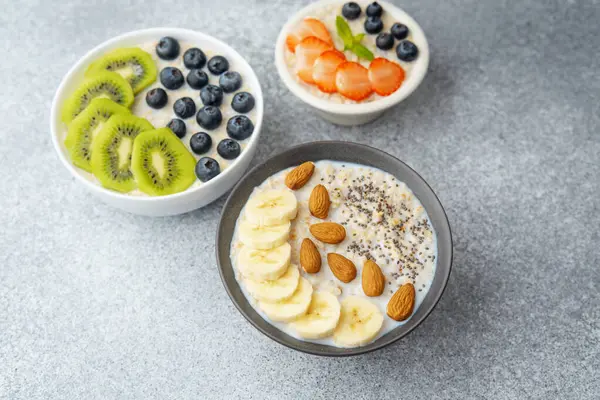 Çeşit çeşit yulaf ezmesi kaseleri ve gri masada fındık ve chia tohumları.