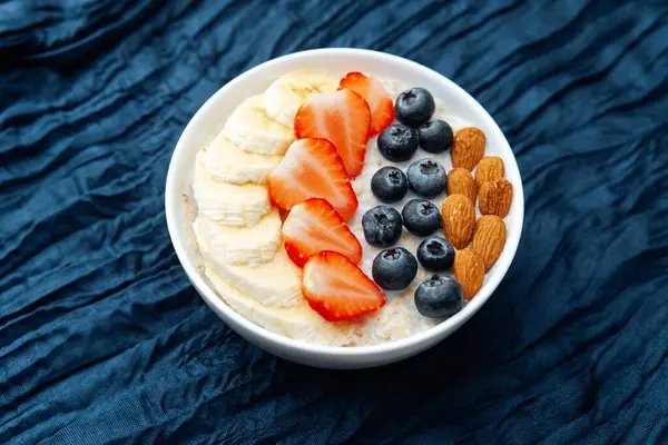 Koyu mavi tekstil arka planında meyveler ve bademlerle yulaf ezmesi kasesi