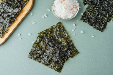 Yeşil arka planda cam kasede tuz bulunan kavrulmuş yosun çerezi.