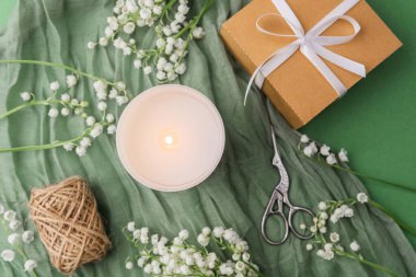 Çiçekli yanan mum ve yeşil kumaşlı hediye kutusu.