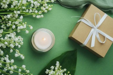Kavanozda mum alevi, vadi çiçekli beyaz zambak ve yeşil arka planda hediye kutusu.