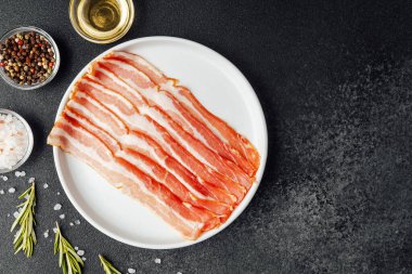 Beyaz tabakta çiğ domuz pastırması, biber, tuz ve biberiye.