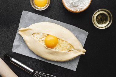 Parşömen üzerinde peynir ve sarısı olan Khachapuri ve koyu mutfak masası.