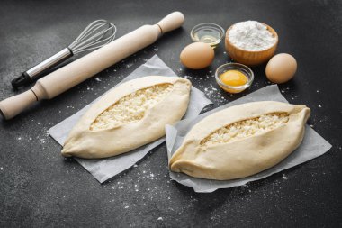 Malzemelerin üst görüntüsü ve iki pişmemiş khachapuri un kaplı siyah masa üzerinde