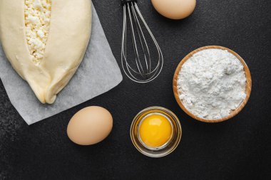 Süzme peynirli çiğ khachapuri ve siyah arka plandaki malzemeler.