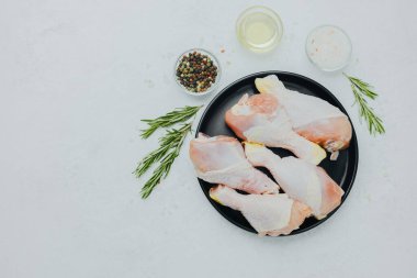 Biberiye ve baharatlı siyah tabakta çiğ tavuk budu.