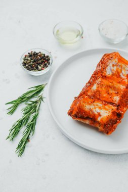 Beyaz tabakta marine edilmiş domuz pirzolası, biberiye ve baharatlı.