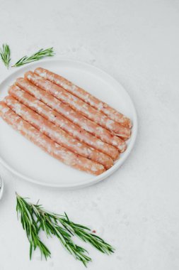 Biberiye ve baharatlı, beyaz tabakta pişmemiş sosisler.