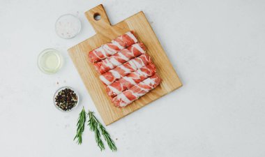 Domuz pastırmasına sarılı sosisli börekler, ahşap tahtada otlarla.