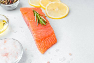 Hafif bir yüzeye yerleştirilmiş somon filetosu. Yanında bitkiler ve limon dilimleri var..